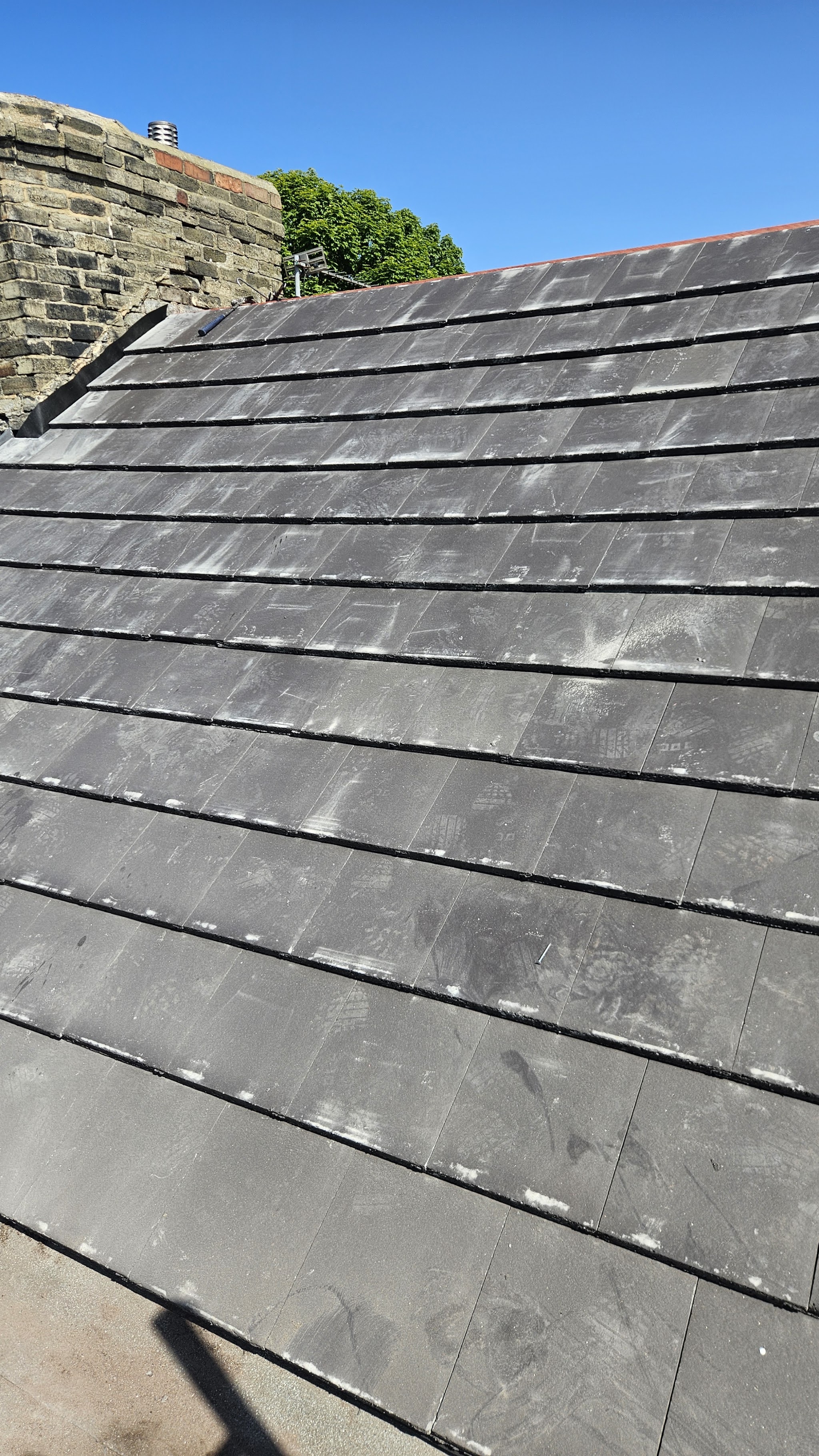 A newly laid slate roof running up to a stone chimney stack