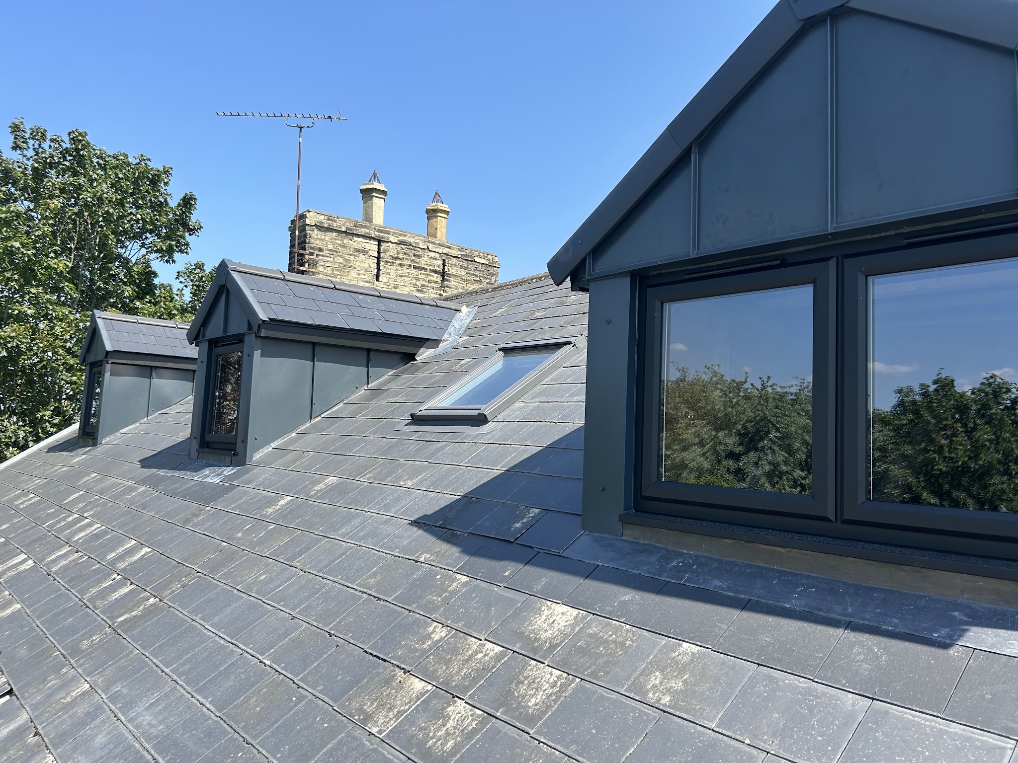 A new slate roof with grey-clad dormer windows and a rooflight under a blue sky