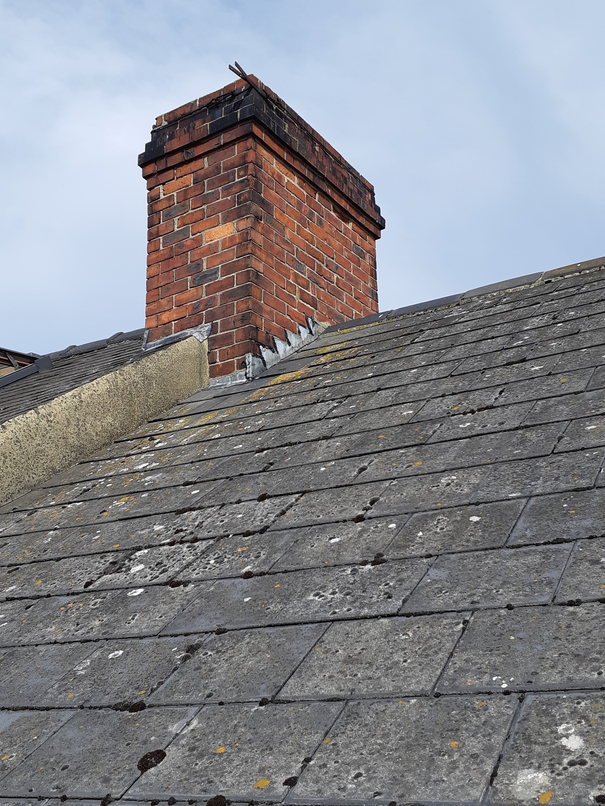 A brick chimney with metal flashing at its base on a slate roof
